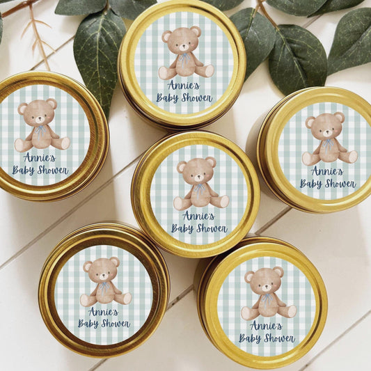 May include: Six gold tins with blue and white gingham labels. Each label features a cartoon brown bear with a blue bow tie. The text on the labels reads &#39;Annie&#39;s Baby Shower&#39;.